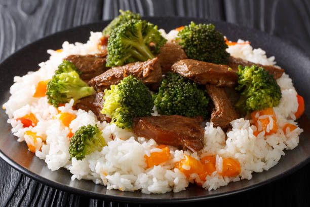 deliciosa carne de res sana con brócoli aderezada con arroz y caqui de cierre en un plato. horizontal - beef rice orange stir fried fotografías e imágenes de stock