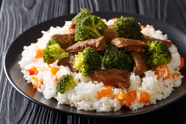 boeuf asiatique avec brocoli servi avec riz et persimmon close-up sur une assiette. horizontal - beef rice orange stir fried photos et images de collection