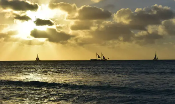 Aruba with a trio of silhouetted sailing sailboats on the horizon.