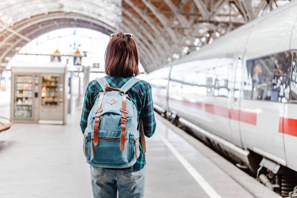 una joven turista con mochila espera el tren en la estación de tren - estación de tren fotografías e imágenes de stock
