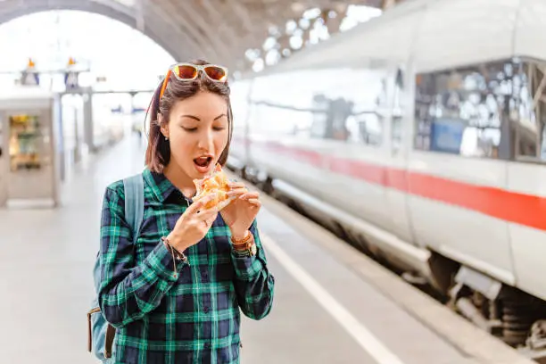 Photo of Healthy young woman biting her hamburger at railway station near fast train