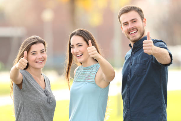 три человека жестикулируя пальцы на улице - thumbs up teenager adolescence group of people стоковые фото и изо�бражения