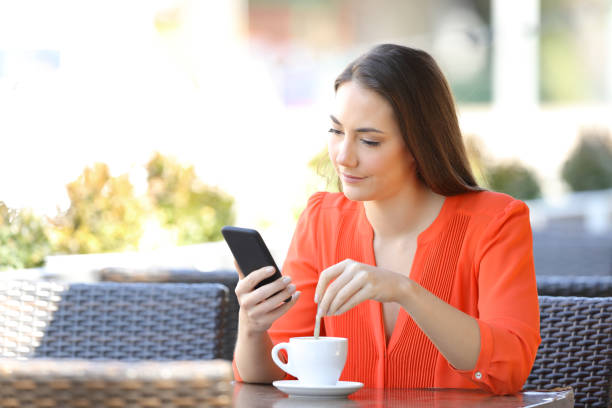 istock Woman stirring coffee checking smart phone in a bar 1145856078