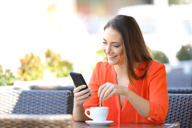 バーでコーヒーをかき混ぜる電話を使って幸せな女性 - 混ぜる ストックフォトと画像