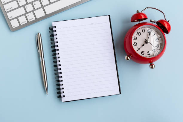 istock Top View of Office Desk With Computer keyboard, Notepad, Coffee, Pen and Red Alarm Clock 1145859313