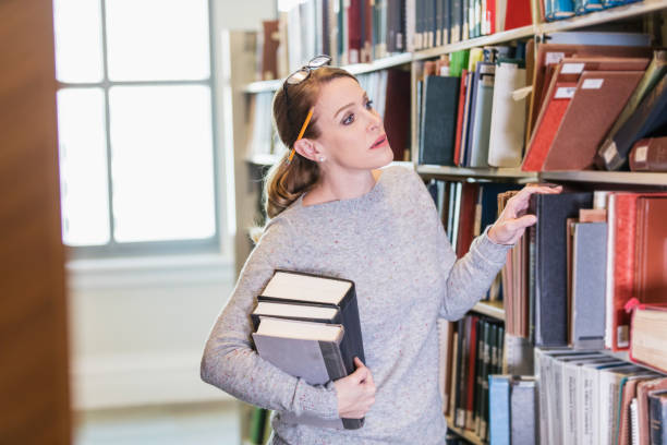 istock Mature woman looking for book in library 1145862342
