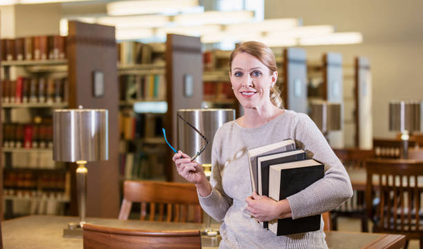kobieta w bibliotece niosąca stos książek - standing mature women professor light zdjęcia i obrazy z banku zdjęć