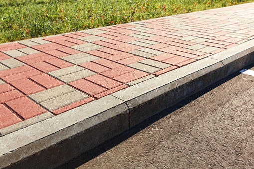 The pavement of red and gray paving stones is separated from the road by a concrete curb.