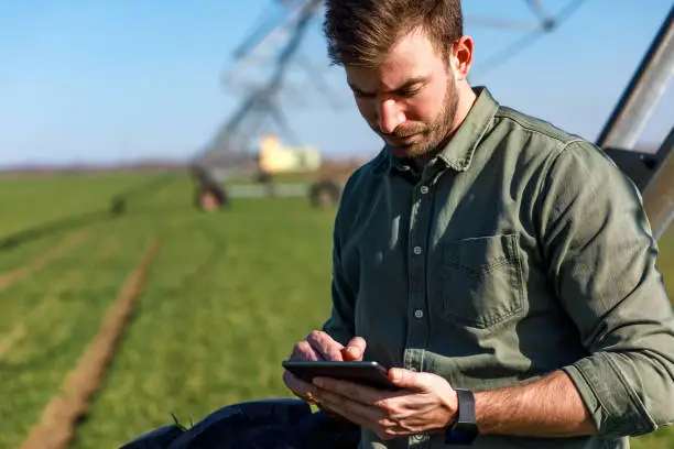 Young farmer standing in wheat field and setup irrigation system on tablet.