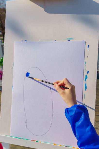 istock Artist's work place. A kid paints with blue gouache a picture. Open air workshop 1145870295