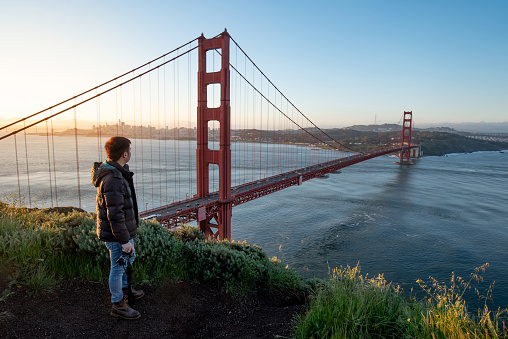 Asian man photographer and tourist enjoy looking at Golden Gate Bridge during sunrise, Iconic bridge and famous landmark of San Francisco, California, USA. Travel photography concept