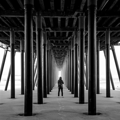 Asian man photographer and tourist taking photo under bridge structure of Pismo pier at Pismo beach, California, USA. Summer vacation travel concept