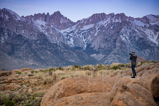 Asian man photographer and tourist taking photo of Mount Whitney landscape at dawn from Alabama Hills in winter season of Lone Pine, California, USA. Travel photography concept