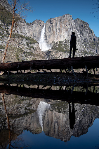 Reflection of Young Asian man photographer and traveler standing on the log enjoy looking at Yosemite falls in Yosemite national park, famous natural attraction in California, USA