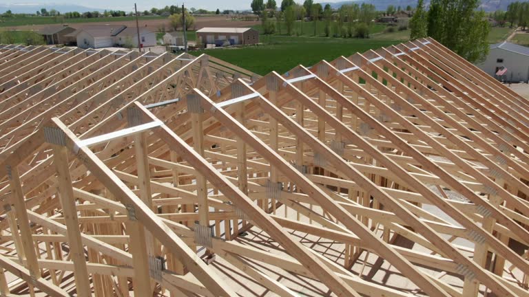 Descending Aerial Drone Shot of a Row of Wooden Roof Trusses of a Framed House on a Construction Site with Construction Workers on a Sunny Day