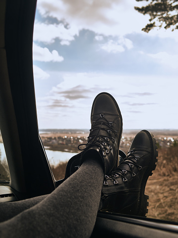 The legs of a woman in gray pantyhose and leather shoes lie on the side window of the car.