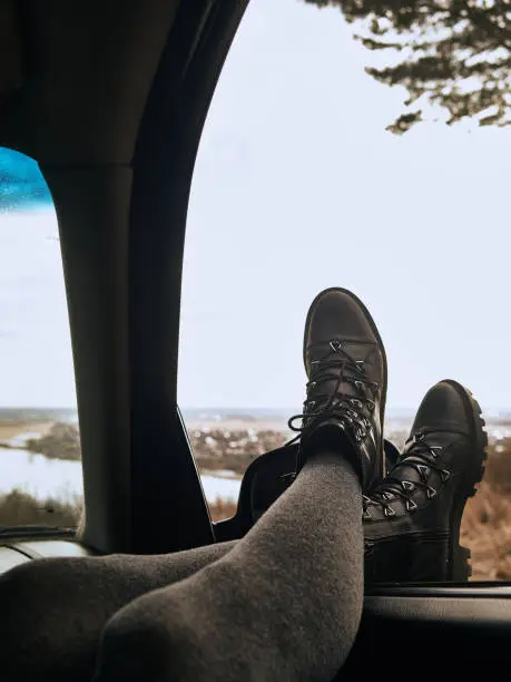 The legs of a woman in gray pantyhose and leather shoes lie on the side window of the car.
