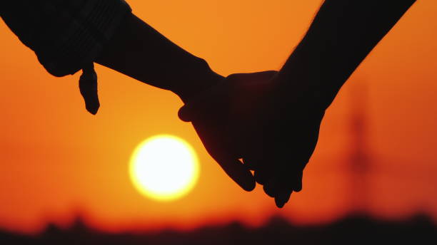 istock Young couple holding hands on the background of a large setting sun 1145885657