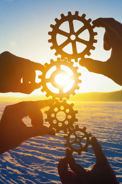 cuatro manos de hombres de negocios sosteniendo engranajes doblados en un mecanismo de puzzle al atardecer. - gear teamwork human hand equipment fotografías e imágenes de stock