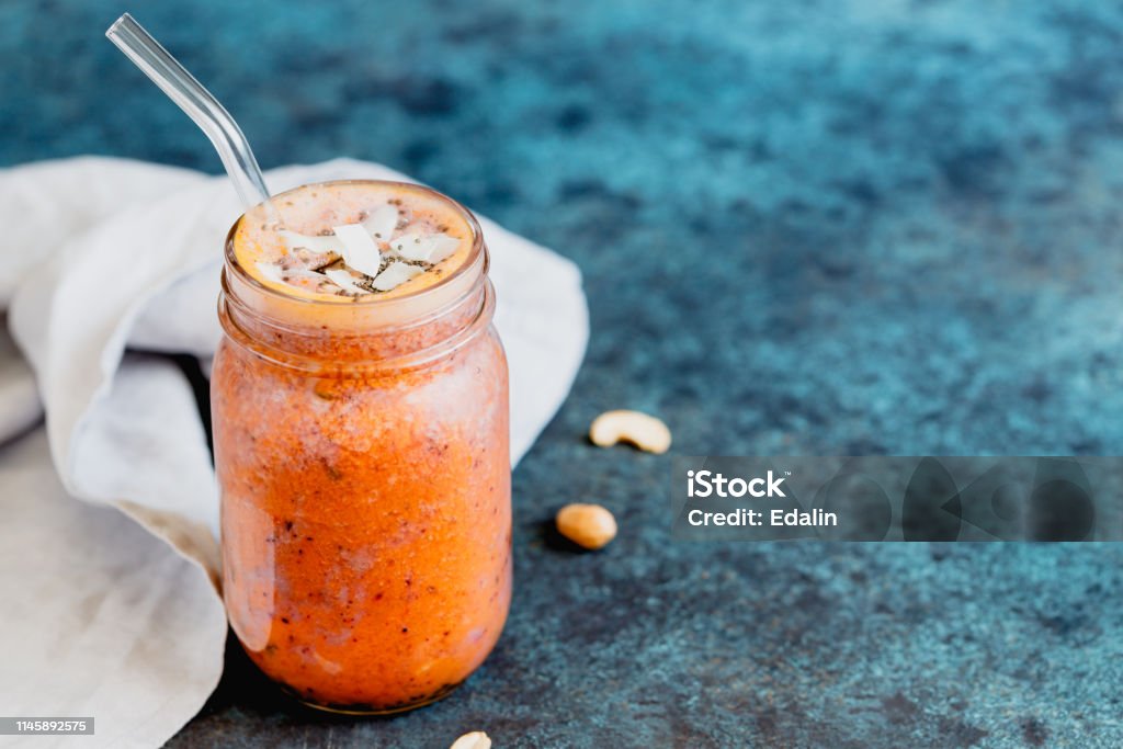 Orange and purple vegan smoothie is made from blueberry, sea buckthorn, coconut cream, nuts and chia on a blue background. The concept of healthy summer food and drink. Above Stock Photo