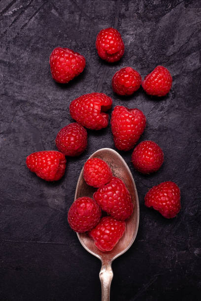 Fresh raspberries, in the foreground, on the rough and dark background.