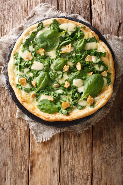 istock Italian cuisine thin pizza with fresh spinach, garlic and cheese close-up on a board. Vertical top view 1145900990