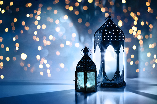Un par de linternas ornamentales marroquíes brillantes en la mesa. Tarjeta de felicitación, invitación para el mes sagrado musulmán Ramadán Kareem. Fondo de noche azul festivo con brillantes luces bokeh doradas. photo