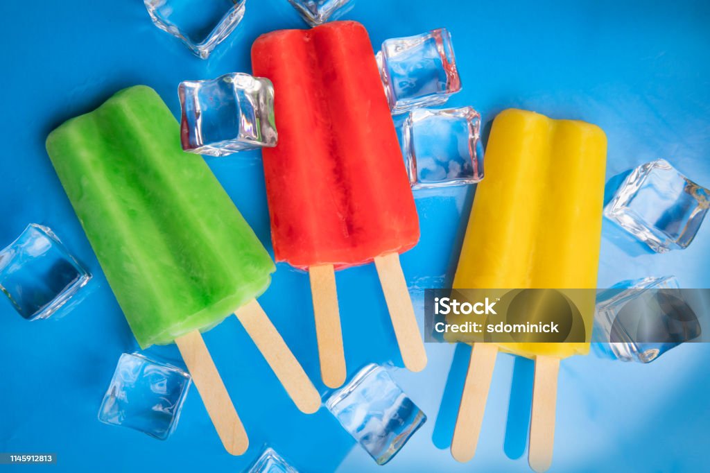 Green Red Yellow Ice Pops on Blue A green, red and yellow ice pop with ice cubes on a reflective blue surface. Close-up Stock Photo