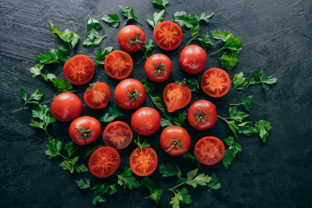 istock Half tomatoes and green parsley around on dark background. Fresh ingredients for making vegetarian salad. Harvested garden vegetables 1145916680