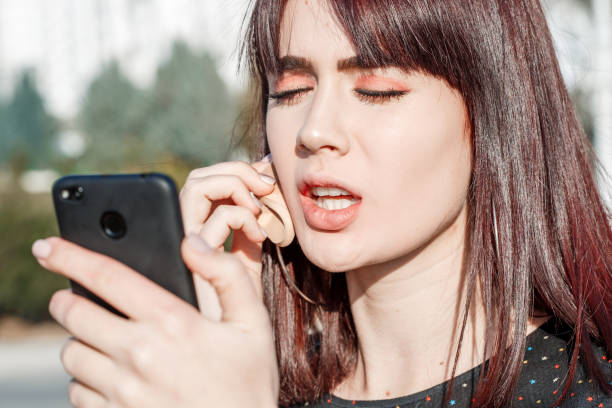istock A young and beautiful woman adjusts her makeup as she uses her smartphone camera as a mirror. She is standing outdoors during the day. 1145917336