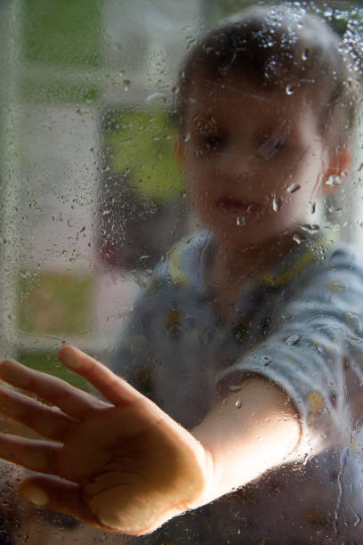 istock boy is touching a wet glass with drops 1145922817