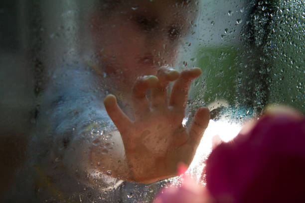 istock boy is touching a wet glass with drops 1145922837