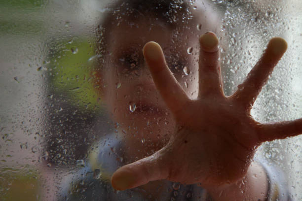 istock boy is touching a wet glass with drops 1145922845
