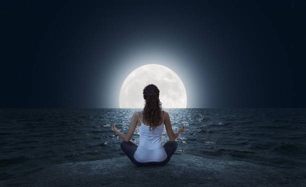 istock Young woman meditating on the beach at full moon 1145924471