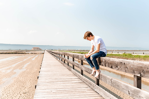 Young caucasian man sitting on a wooden fence by the salt pans.