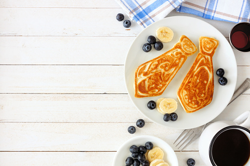 Tie shaped pancakes with blueberries and bananas. Fathers Day brunch concept. Above view side border on a white wood background.