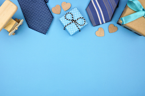 Fathers Day top border of gifts, ties and hearts on a blue background. Top view with copy space,