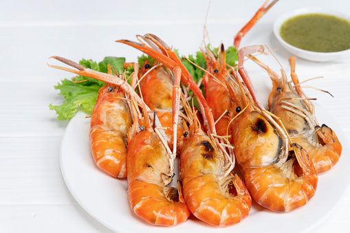 Burned shrimp Or Grilled shrimp and seafood sauce is very tasty on a white plate on white wood background.