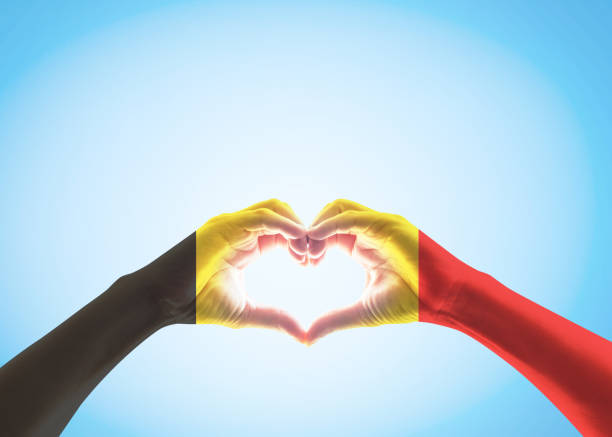 istock Belgian black yellow red flag pattern on people heart shaped hands (clipping path) on sky background 1145942640
