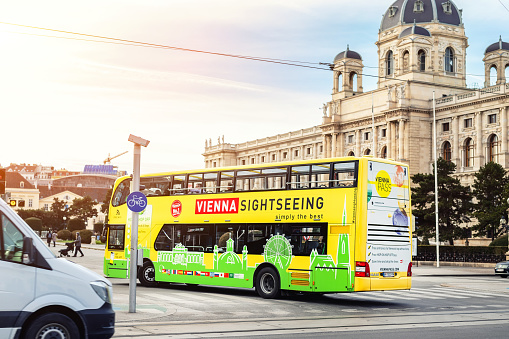 Vienna, Austria - January 16th,2019:Funny green-yellow doubledecker touristic sightseeing bus going along Vienna old city center on bright sunny day.Austrian history museum building on background.