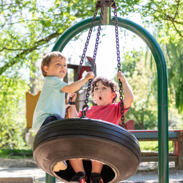 Laughing Three years old children, one hispanic and one caucasian, playing in the park playground swing