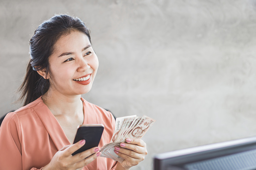 mujer asiática feliz mano sosteniendo teléfono inteligente y billetes photo