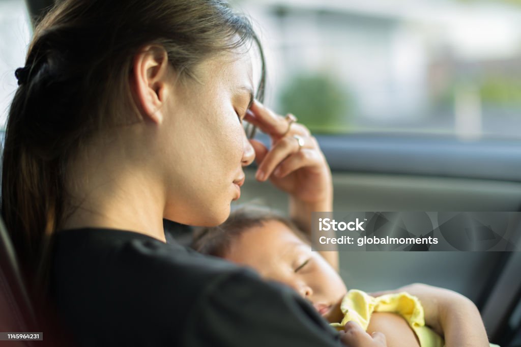 Tired stressed mother holding her baby. A unhappy exhausted mom trying to take a nap with her baby in the car. Mother Stock Photo