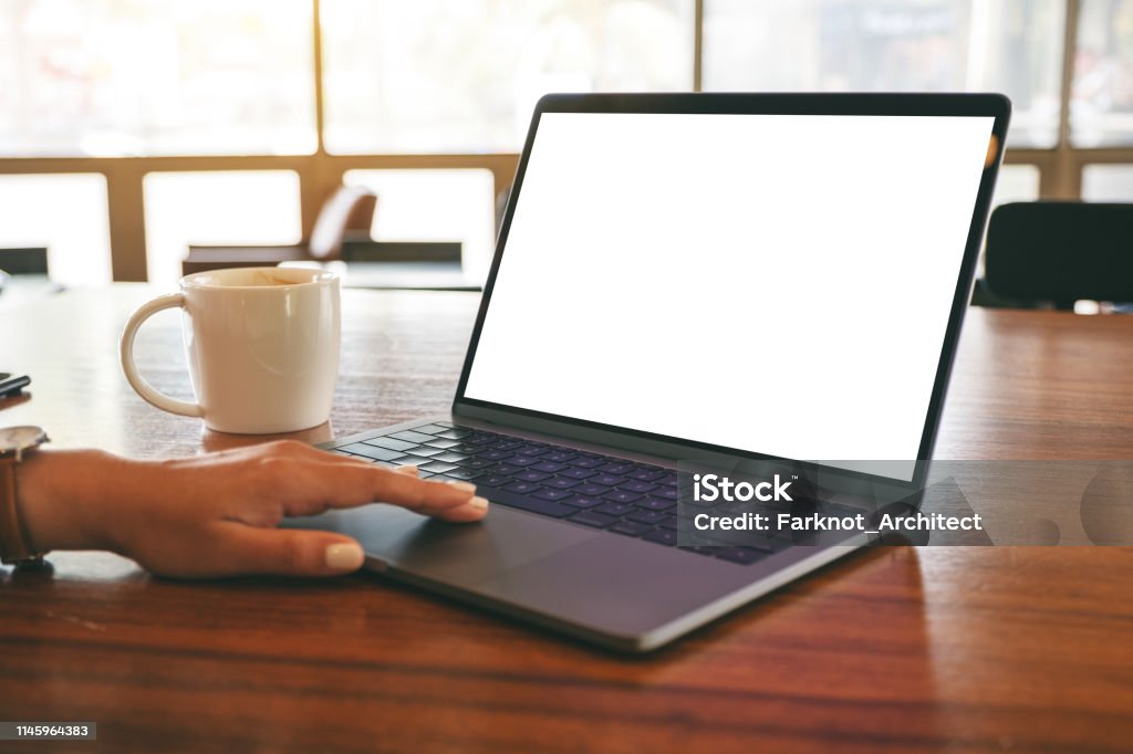 a woman's hand using and touching on laptop touchpad with blank white desktop screen Mockup image of a woman's hand using and touching on laptop touchpad with blank white desktop screen with coffee cup on wooden table Above Stock Photo