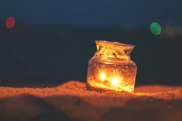 Closeup image of a glass bottle candles holders on the beach at night