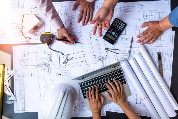 istock engineers pointing to building on blueprint and using laptop to drawing design building Project in office, construction concept. Engineer concept 1145964587