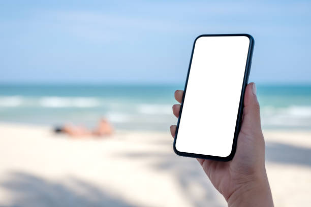 istock woman's hand holding black mobile phone with blank desktop screen by the beach 1145965385