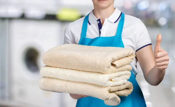 Photo of A laundry worker with clean towels showing a positive gesture.