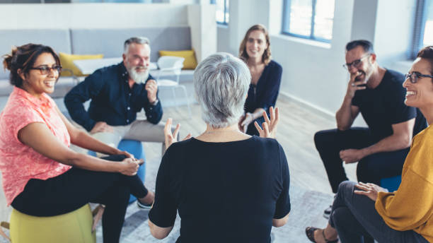 Business team sitting in circle and discussing Group of business people sitting in circle and discussing in the office. Mature woman talking with coworkers in a team building session. activity stock pictures, royalty-free photos & images