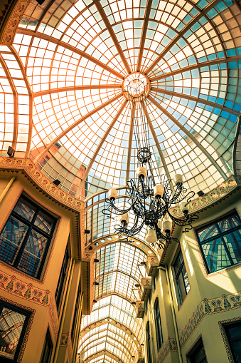 Color image depicting a stained glass ceiling and elegant chandelier in Oradea, a city in the Transylvania region of Romania. **IMAGE SHOT IN A PUBLIC WALKWAY, FREELY ACCESSIBLE TO THE PUBLIC, IN ORADEA, ROMANIA, WHERE THERE ARE NO COPYRIGHT RESTRICTIONS**. Room for copy space.